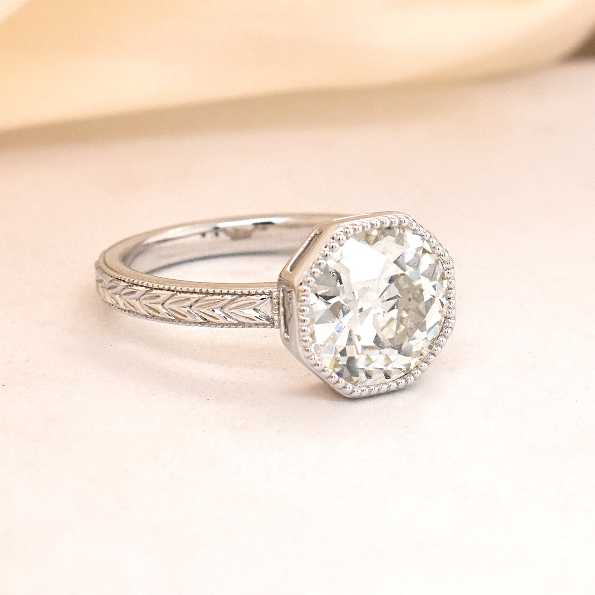 Round White Diamond Set in an Octagon Bezel on a Leaf Detail Engraved Band in White Gold